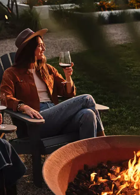 Women sitting next to a fire pit, smiling, holding a glass of red wine.