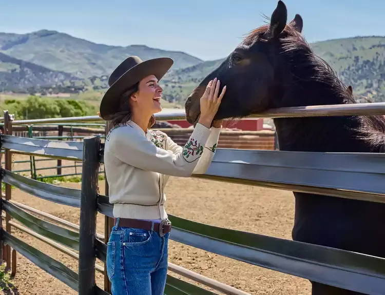 Smiling women standing and holding the muzzle of a horse inside a ranch pen