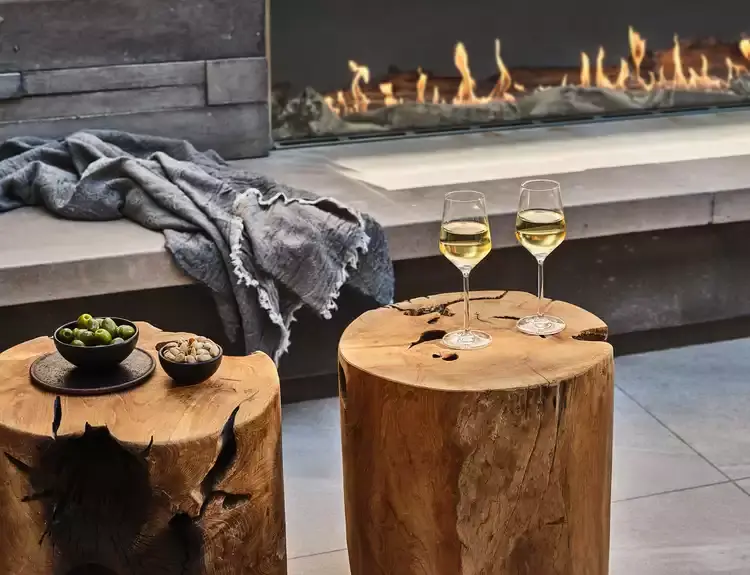 Two rustic tables made out of tree stumps stand next to a modern fireplace.